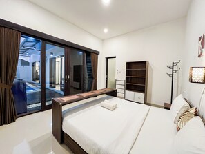 A modern bedroom with a large bed, a wooden nightstand, a wardrobe, and a sliding glass door leading to a balcony. - 2Br Jwk Bali Private Pool Villa Near Pandawa Beach (Kutuh)