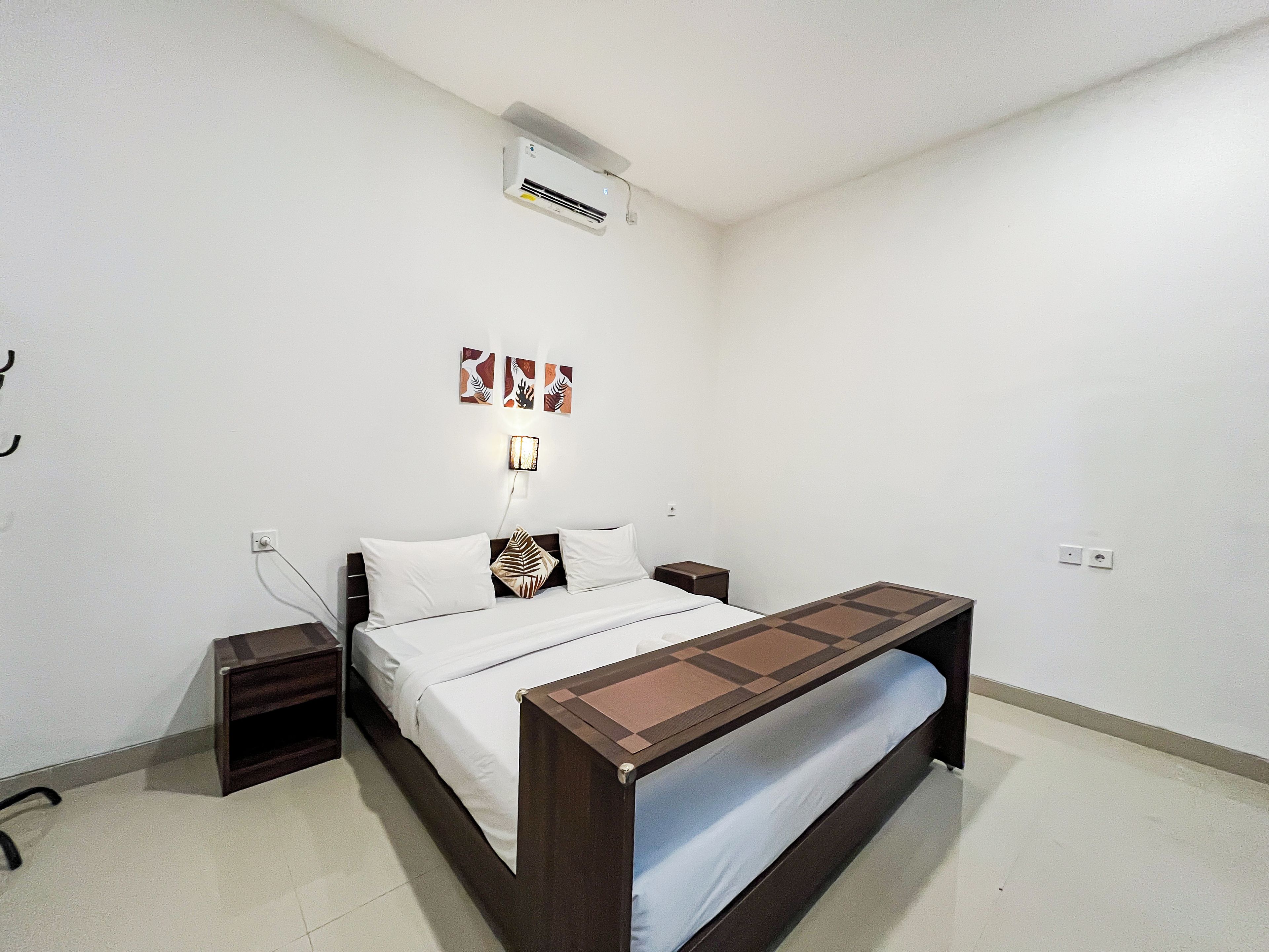 A bedroom with a bed, bedside tables, a wall-mounted air conditioner, and a wall-mounted lamp.
