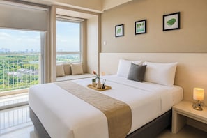 A hotel room with a large bed, a bedside table with a lamp, a window with a view of the city, and three framed pictures on the wall. - Polished And Sleek Studio (No Kitchen) At Apartment Mustika Golf Residence (Cikarang)