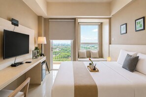 Ein Hotelzimmer mit Bett, Schreibtisch mit Fernseher, Fenster mit Stadtblick und Balkon.