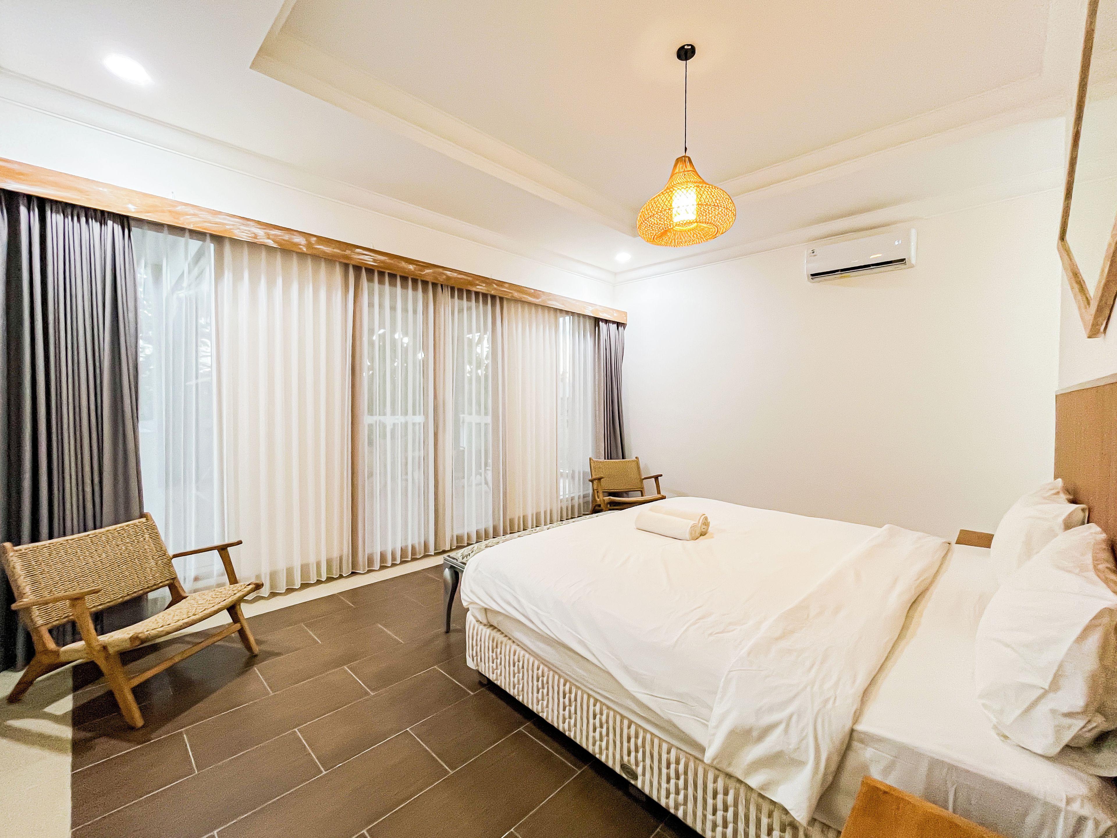 Habitación de hotel con cama, una silla, una ventana con cortinas y una lámpara colgante.