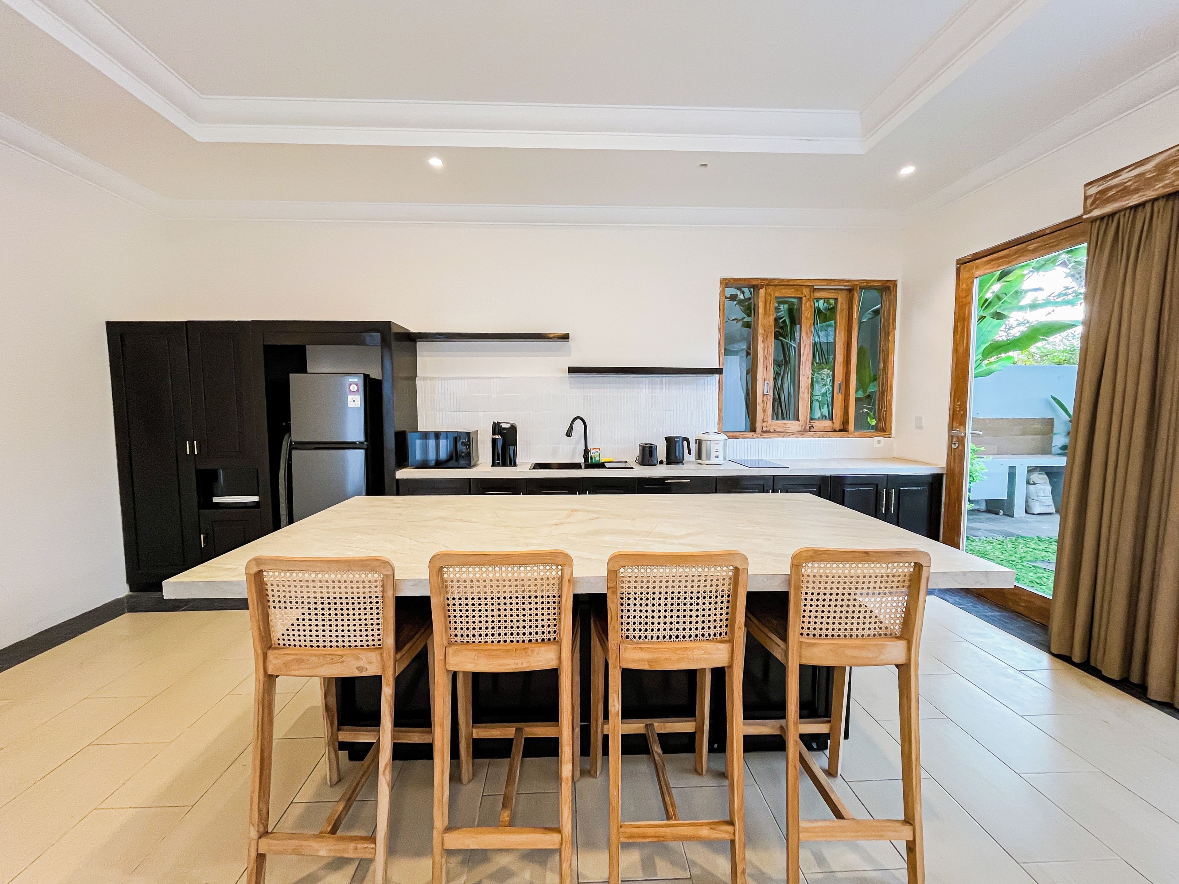A modern kitchen with a large island, four bar stools, and a view of the outdoors.