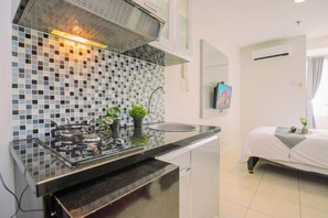 A modern kitchen with a gas stove, a sink, and a tiled backsplash. - Great Choice Studio At Apartment Cinere Bellevue Suites (Depok)