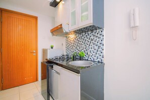 A compact kitchen with a wooden door, a gas stove, a sink, and a tiled backsplash. - Great Choice Studio At Apartment Cinere Bellevue Suites (Depok)