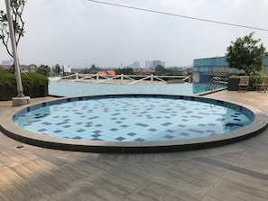A swimming pool with a tiled deck, surrounded by a fence and trees. - Great Choice Studio At Apartment Cinere Bellevue Suites (Depok)