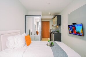 A hotel room with a bed, a TV, a small kitchen area, and a bathroom visible through an open door. - Great Choice Studio At Apartment Cinere Bellevue Suites (Depok)