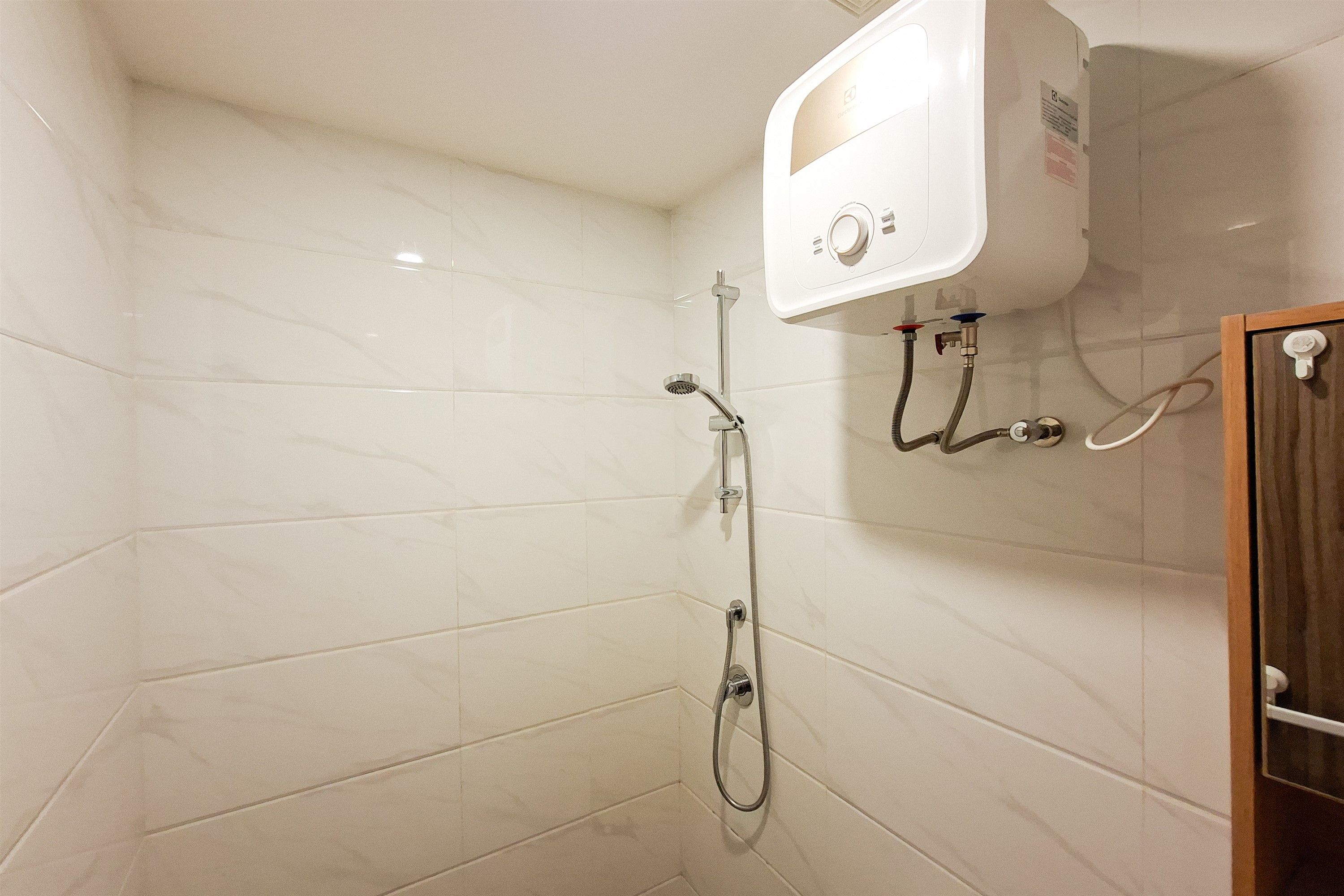Ein Badezimmer mit weiß gefliesten Wänden, einer Dusche inklusive Handbrause und einer Bedienkonsole über der Dusche.