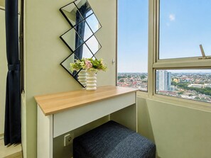 A room with a desk, a mirror, a window with a city view, and a small bench. - Roomy And Warm 3Br At Apartment Nifarro Park (Jakarta)