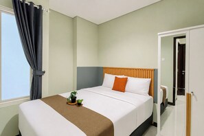 A hotel room with a bed, a potted plant, and a window with curtains. - Roomy And Warm 3Br At Apartment Nifarro Park (Jakarta)