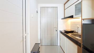 A narrow kitchen with a wooden door, a bench, and a refrigerator.