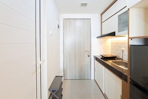 Una cocina estrecha con una puerta de madera, un banco y un refrigerador.