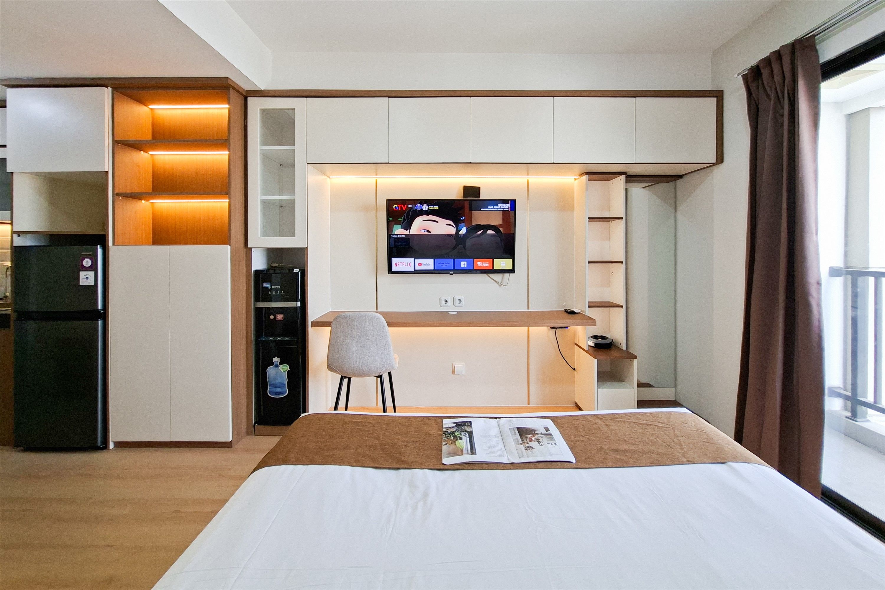 Una habitación de hotel con cama, escritorio, silla, televisor montado en la pared y un mini bar.