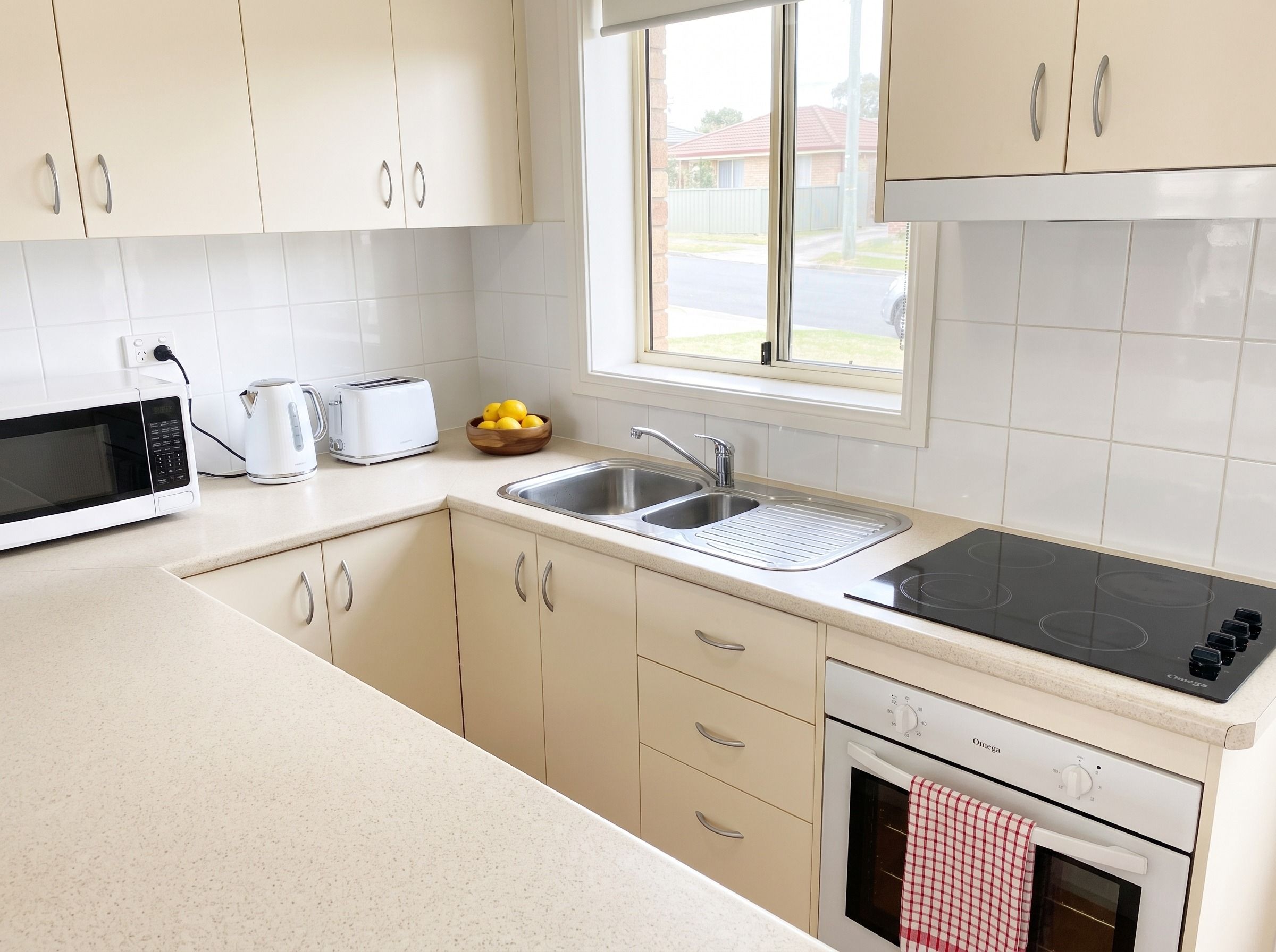 A modern kitchen with white cabinets, a stainless steel sink, a black induction cooktop, a microwave, and a toaster.