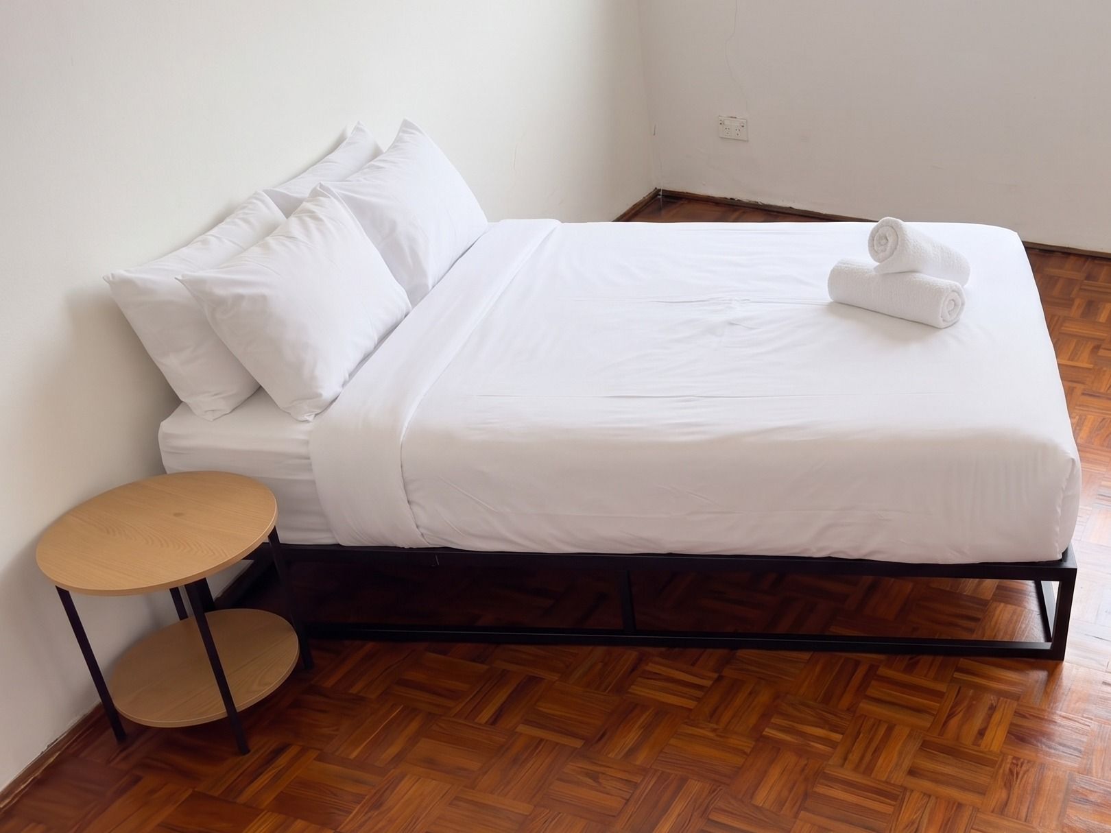 A single-bed room with a wooden floor, a small round table, and a neatly made bed with white bedding.