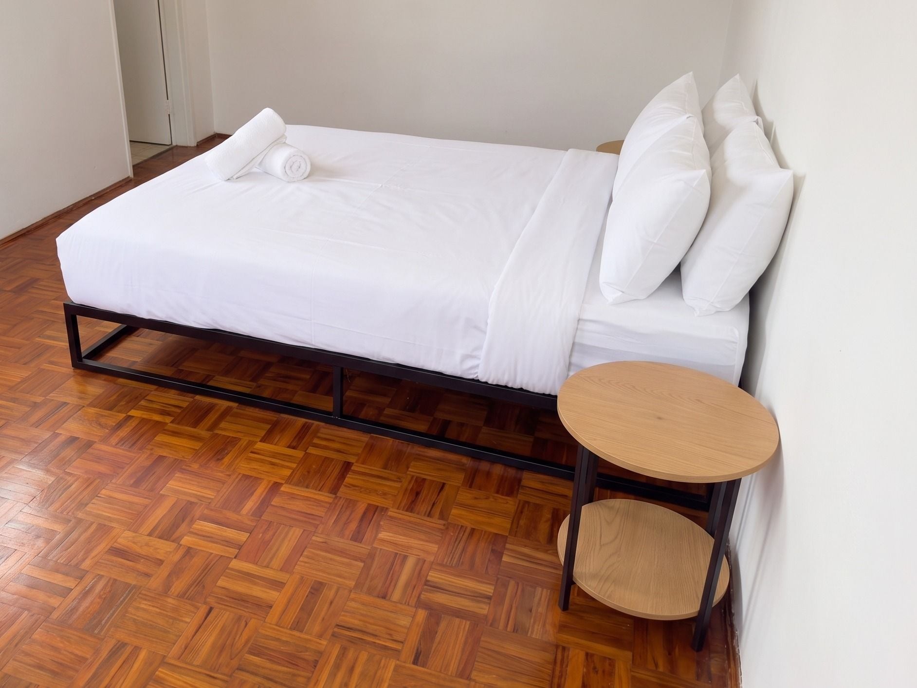A single bed with a wooden frame, white bedding, and a small round table beside it.