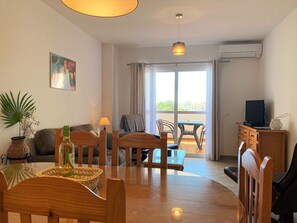 Ein möbliertes Wohnzimmer mit Esstisch, Stühlen, einer Couch, einem Fernseher und einem Balkon mit Blick.