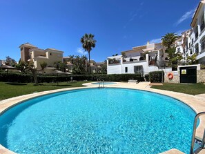 Ein Swimmingpool, umgeben von Gebäuden mit Balkonen, einer Palme und einem Rettungsring an der Wand.