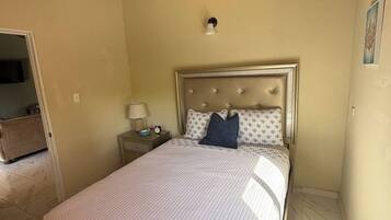 A bedroom with a bed, a nightstand, a lamp, and a wall-mounted air conditioning unit.