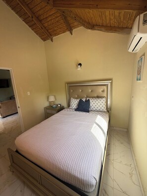 A bedroom with a bed, a nightstand, a lamp, and a wall-mounted air conditioning unit. - Luxurious 5-bedroom House With Private Pool in Cabrera (Cabrera)