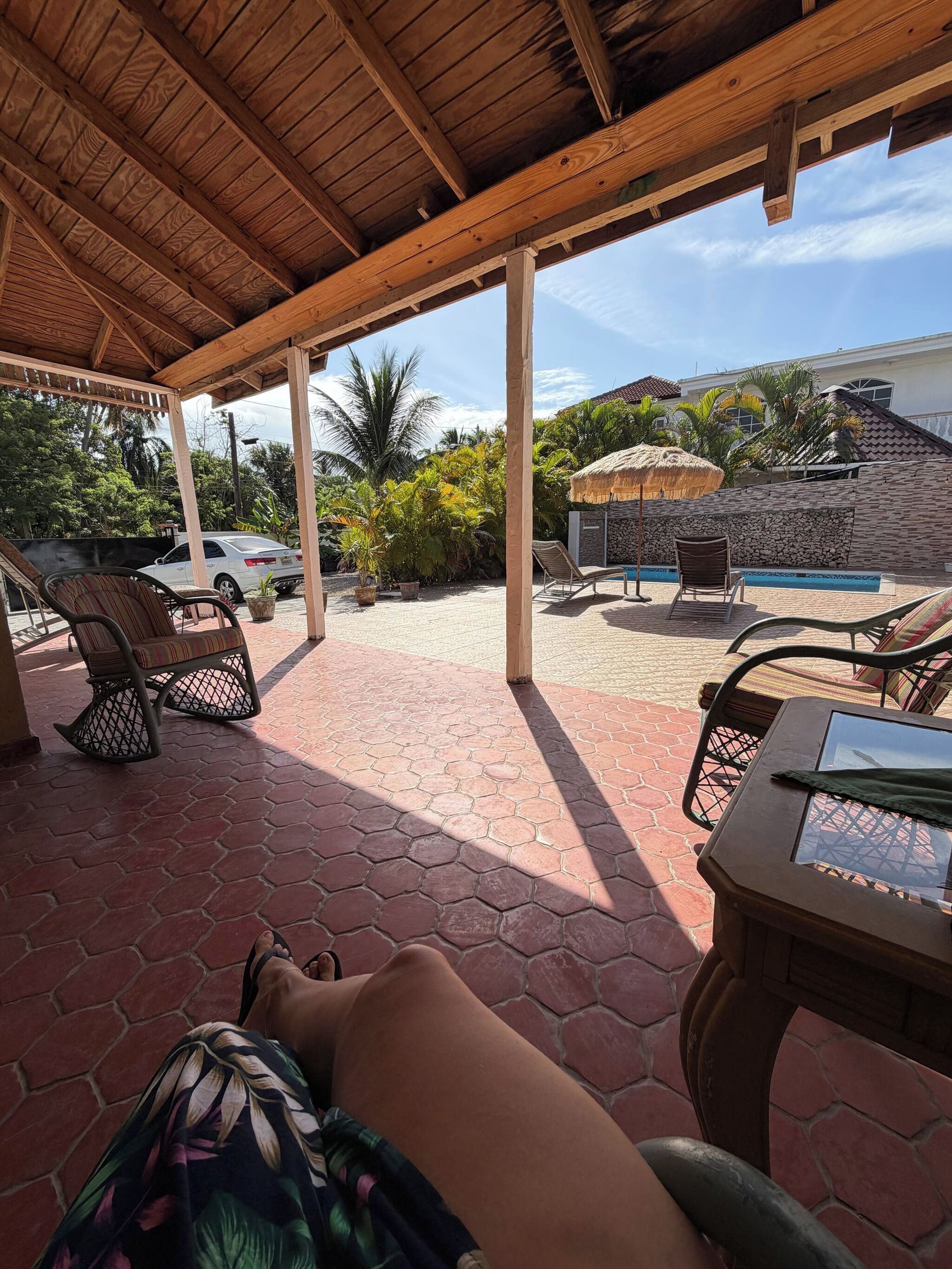 A covered outdoor area with hexagonal tiles, lounge chairs, a pool, and a thatched umbrella.