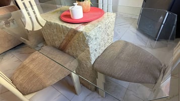 A dining area with a marble-tiled floor, a glass table, and white chairs with cushioned seats.