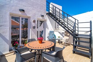 Eine Terrasse im Freien mit einem runden Tisch und Stühlen, einem Blumentopf und einer Treppe, die zu einer oberen Ebene führt.