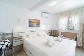 Ein Hotelzimmer mit Bett, Nachttisch, Stuhl, einem Fenster mit Vorhängen und einem Bild an der Wand.