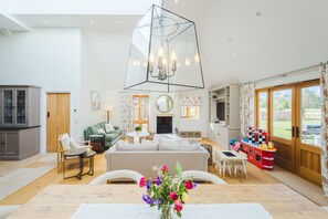 A spacious living area with a high ceiling, a dining table, a sofa, and a children's play area. - The Old Stables - Cotswolds Country Retreat With Shepherd s Hut (Swindon)