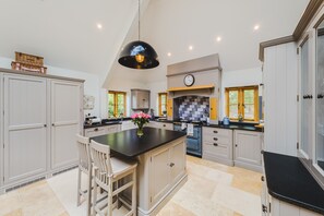 A spacious kitchen with a central island, white cabinetry, a black countertop, and a hanging pendant light. - The Old Stables - Cotswolds Country Retreat With Shepherd s Hut (Swindon)