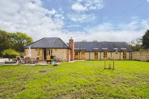 A stone house with a patio, outdoor seating, and a grassy yard. - The Old Stables - Cotswolds Country Retreat With Shepherd s Hut (Swindon)