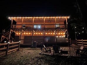 Ein zweistöckiges Holzhaus mit einem Balkon, Lichterketten und Außenbestuhlung.