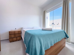 Un dormitorio con una cama, una mesita de noche de madera y una ventana con cortinas.