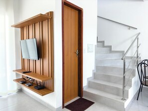 A modern interior with a wooden entertainment unit, a flat-screen TV, a staircase with metal railings, and a door. - Duplex Apartment 5 with 2 Suites 450m from the Beach in Santa Cruz Cabrália (Santa Cruz Cabrália)
