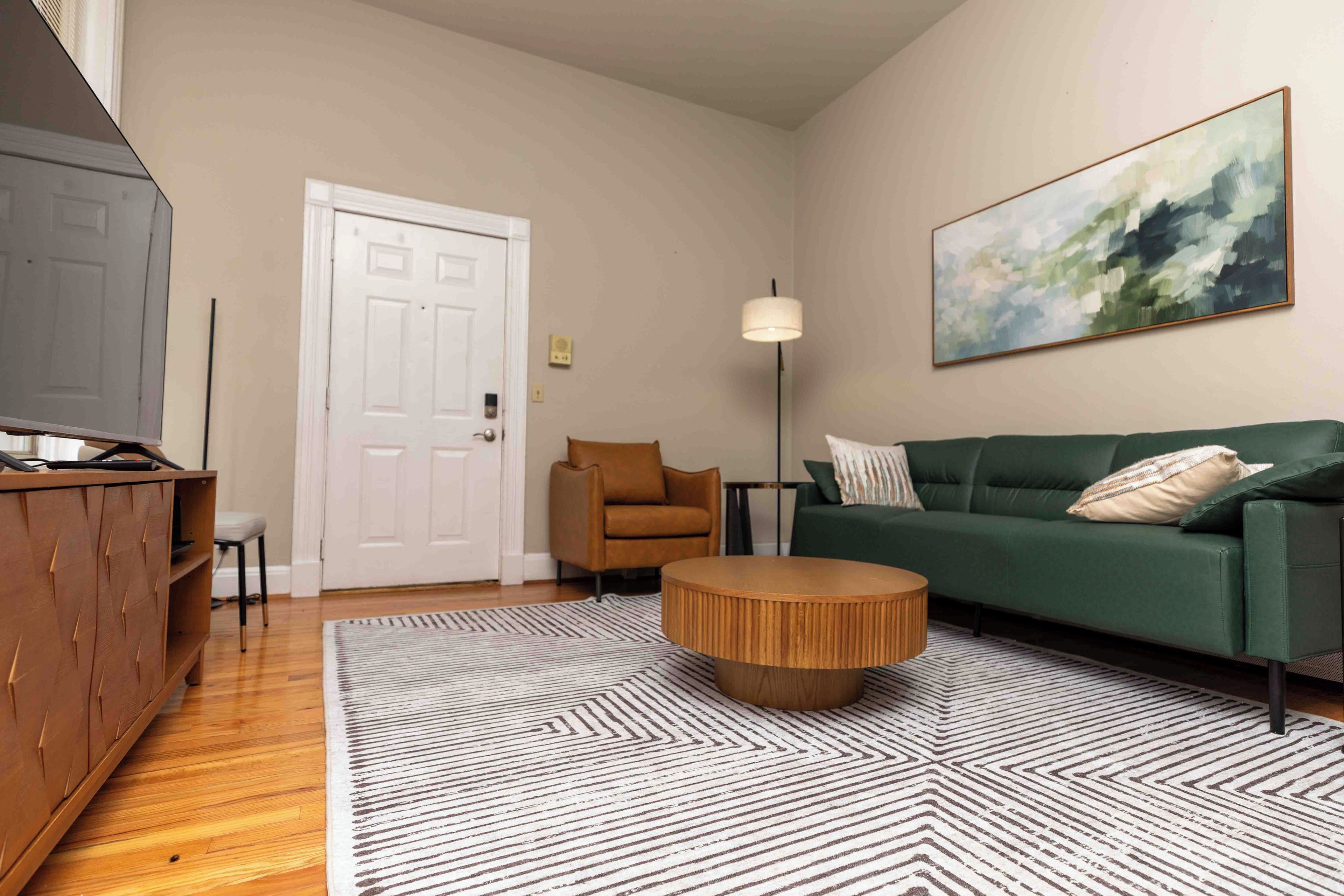 A living room with a green sofa, a wooden coffee table, a striped rug, a brown armchair, and a painting on the wall.