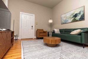 A living room with a green sofa, a wooden coffee table, a striped rug, a brown armchair, and a painting on the wall. - Newly furnished 2BR Apt-Walkable + Near hospitals & universities + Ample Parking (Cincinnati)