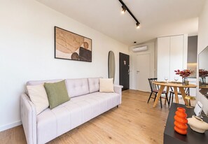 A modern living room with a light-colored sofa, a dining area with a wooden table and chairs, and a kitchen visible in the background. - Krysiewicza Old Town Studio (Poznań)