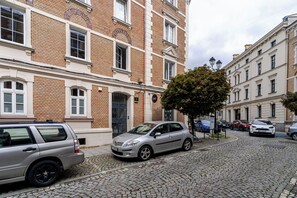 A cobblestone street with parked cars and a building with a brick facade and white trim. - Krzywa Comfort Apartment (Katowice)
