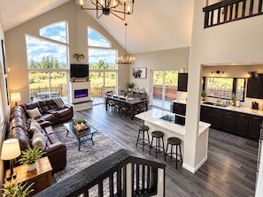 A spacious living area with a fireplace, a dining table, and a kitchen with bar stools. - Massive Family Getaway with private apartment, hot tub and pool table. (Bend)