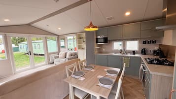 A modern kitchen with a dining area, a built-in oven, and a large window overlooking a green outdoor area.