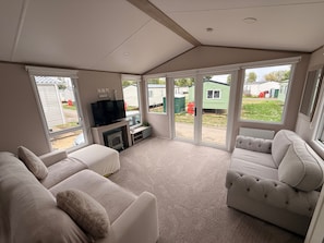 A spacious living area with a fireplace, comfortable seating, and large windows offering views of a residential area. - Cabin Sleeps 6 with Lake Access Parking (Northampton)
