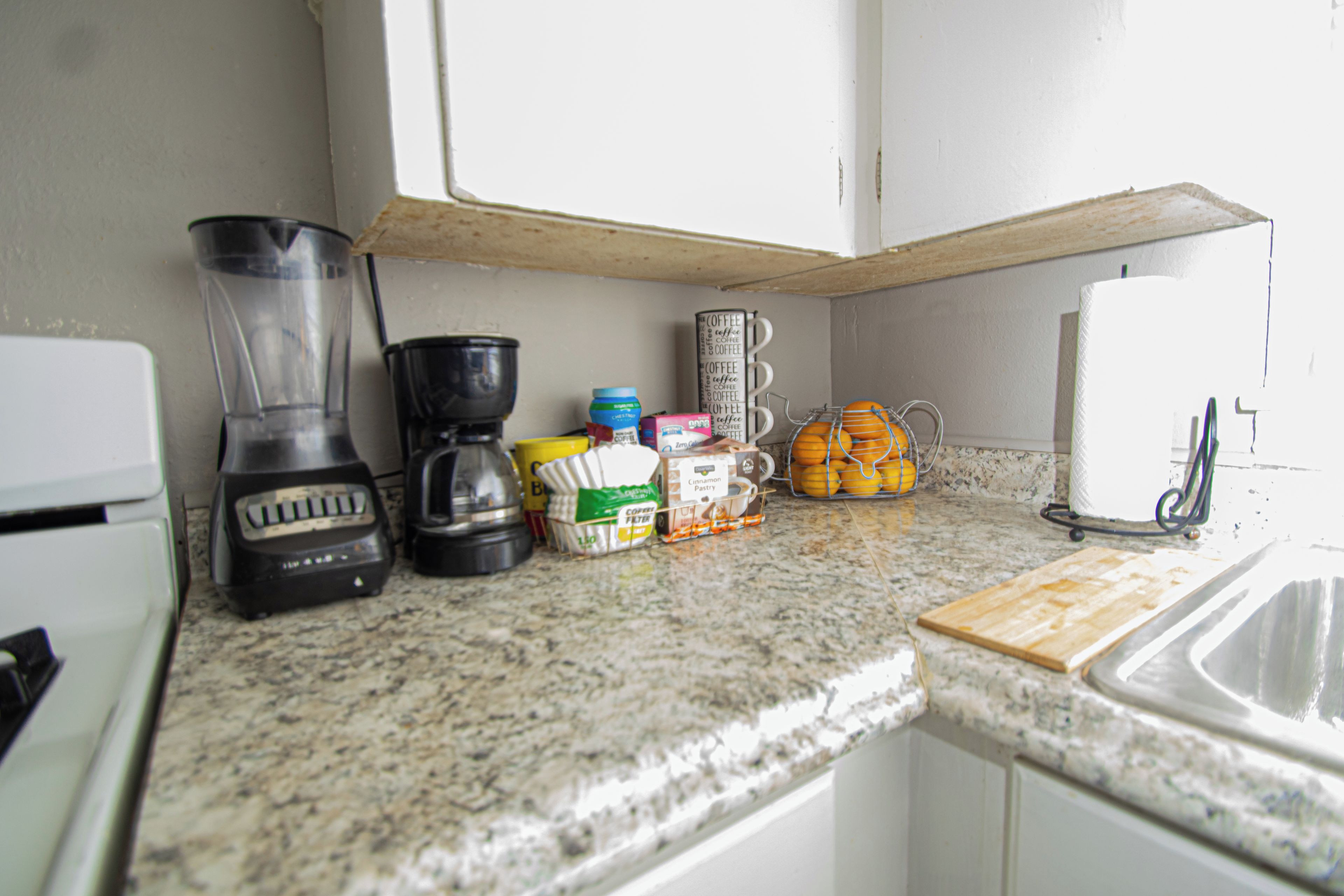 Uma cozinha com liquidificador, cafeteira, ralador de laranja e tábua de corte.