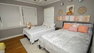 Quarto com duas camas de solteiro e uma cama maior, ventilador de teto e arte decorativa nas paredes.