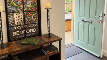 Una obra enmarcada de Bedford, Reino Unido, una consola de madera con libros, una vela y una puerta con cerradura Yale.