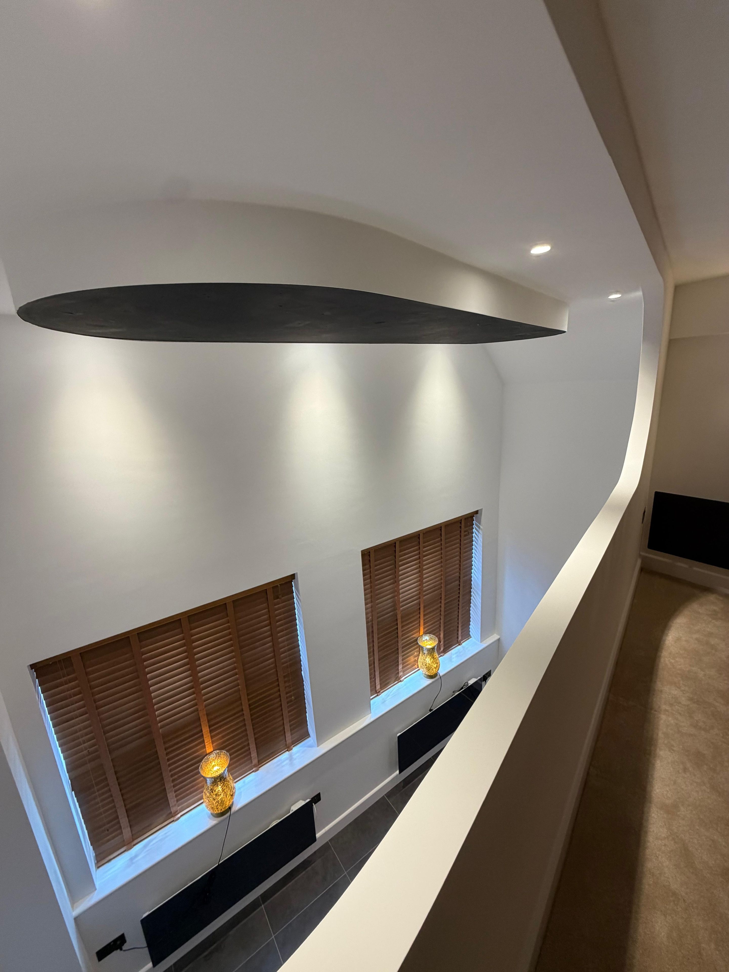 A modern interior with a curved ceiling, recessed lighting, and two windows with wooden shutters.