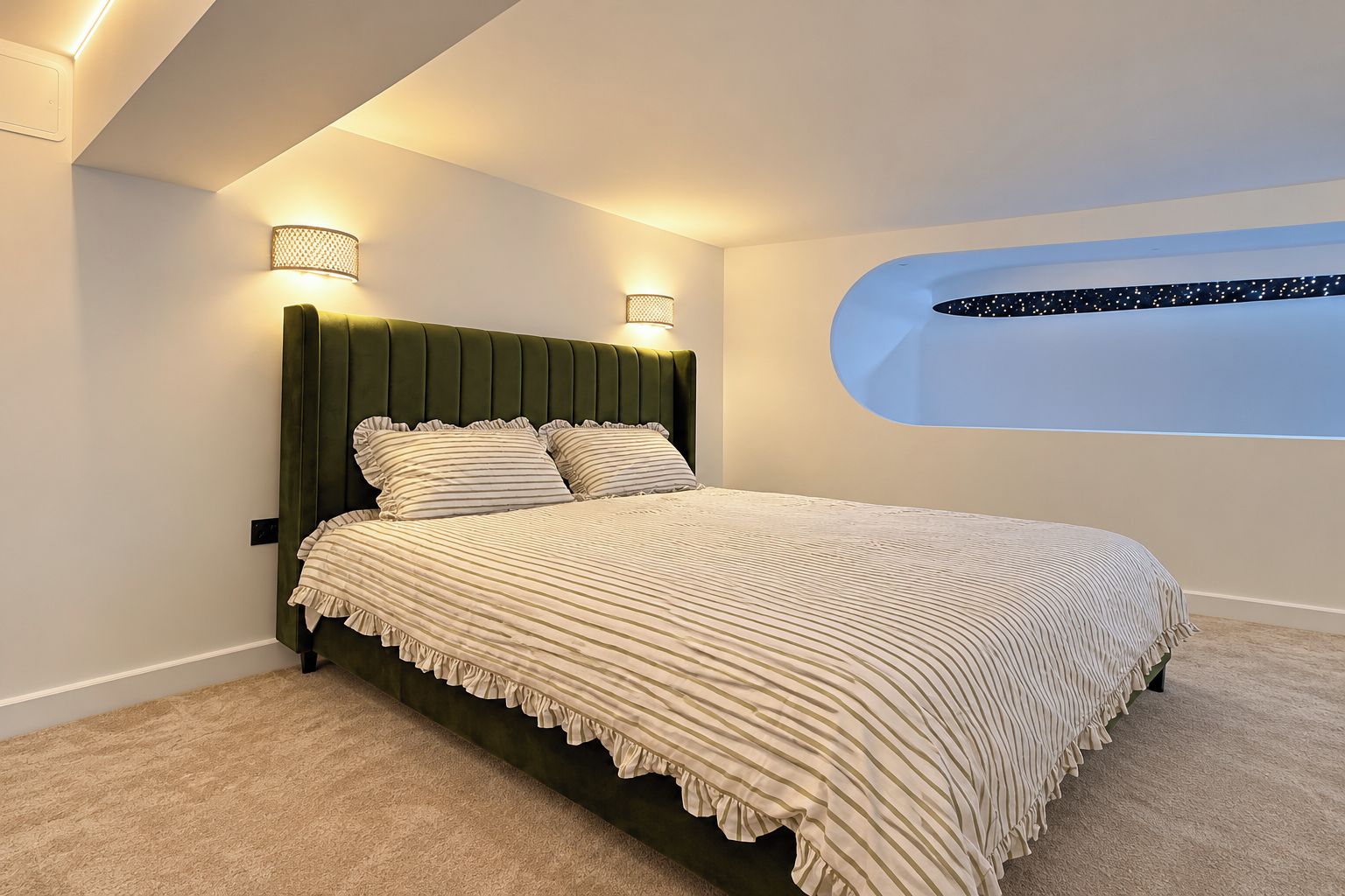 Un dormitorio con cama, dos luces fijadas a la pared, ventana con vistas y cabecera verde.