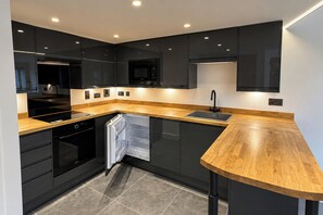 Una cocina moderna con armarios negros, encimera de madera y electrodomésticos integrados.