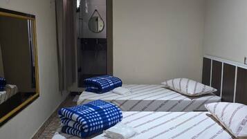 A hotel room with two beds, a mirror, an air conditioning unit, and a bathroom with a shower.