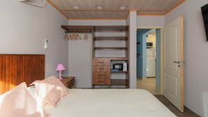 Quarto com cama, mesa de cabeceira, luminária, guarda-roupa e porta que dá para uma cozinha.