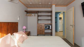 Un dormitorio con cama, mesita de noche, lámpara, armario y una puerta que da a una cocina.