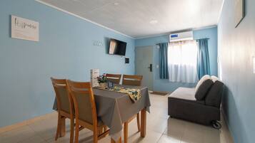 Un comedor con mesa y sillas, un sofá, un televisor en la pared y una ventana con cortinas.